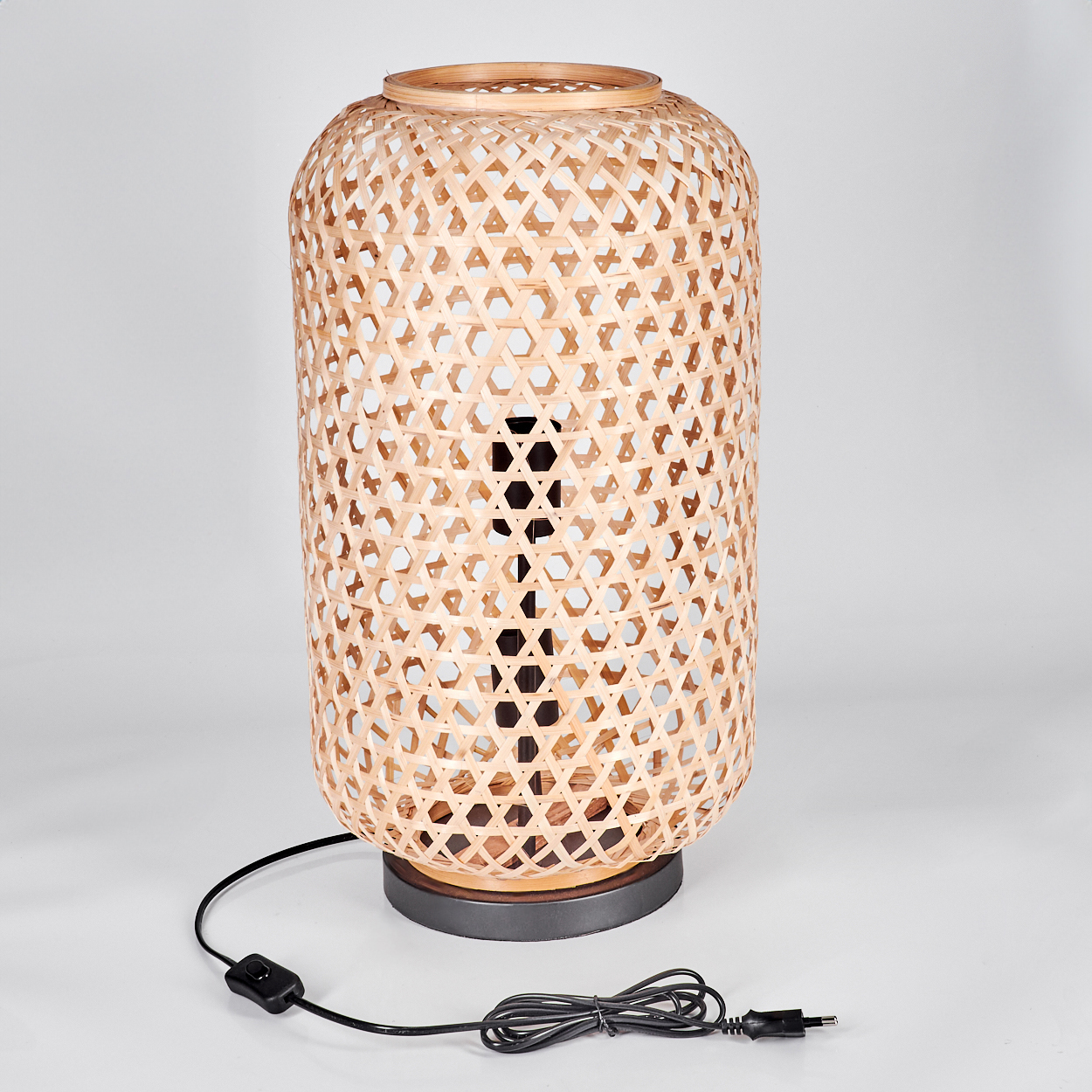 Eine gewebte Bambuslampe auf grauem Sockel. Ein schwarzes Kabel mit Schalter und Stecker geht von der Lampe aus.