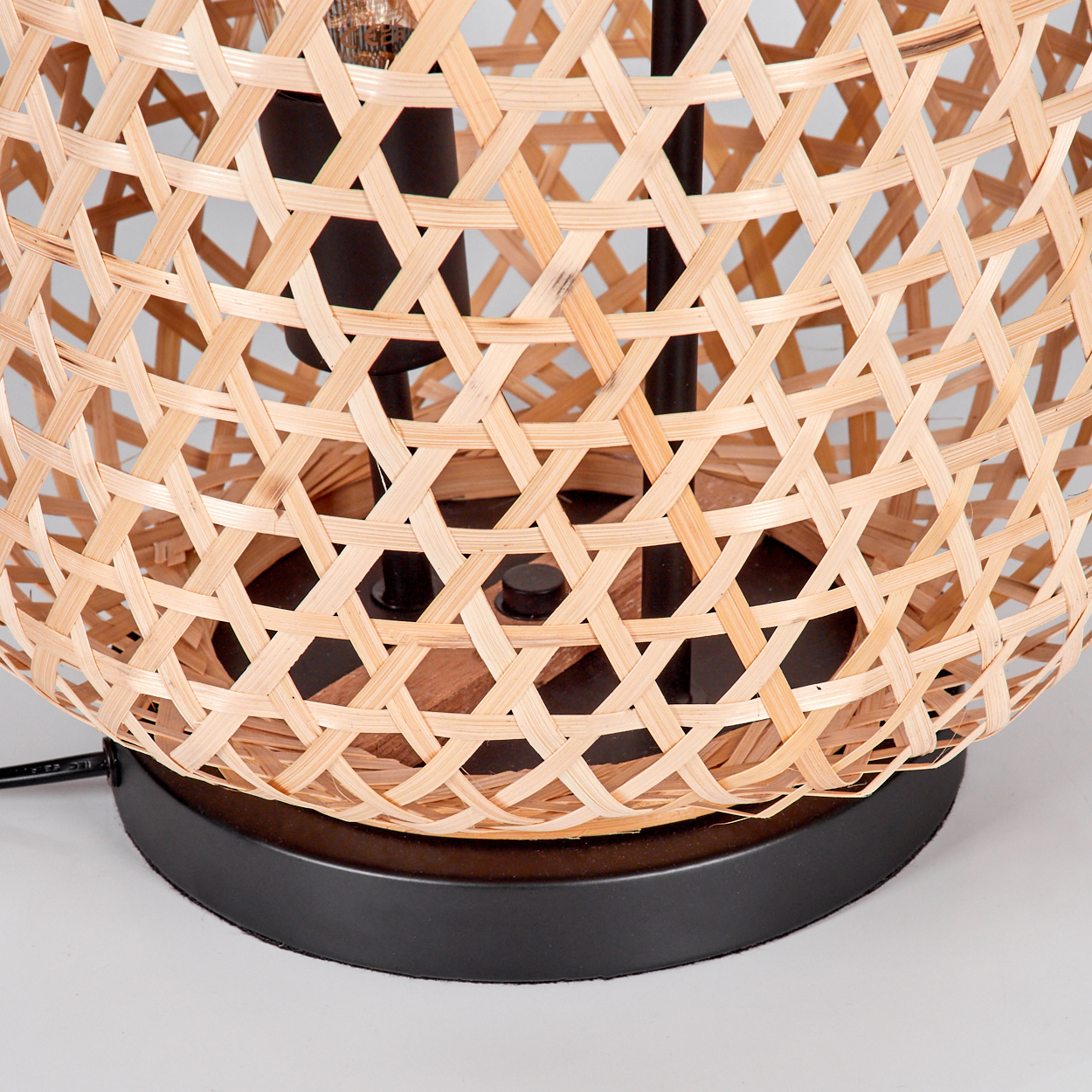 Nahaufnahme einer Lampe. Sie hat einen Lampenschirm aus gewebtem Bambus mit schwarzen Metallstützen und -fuß auf weißem Untergrund.
