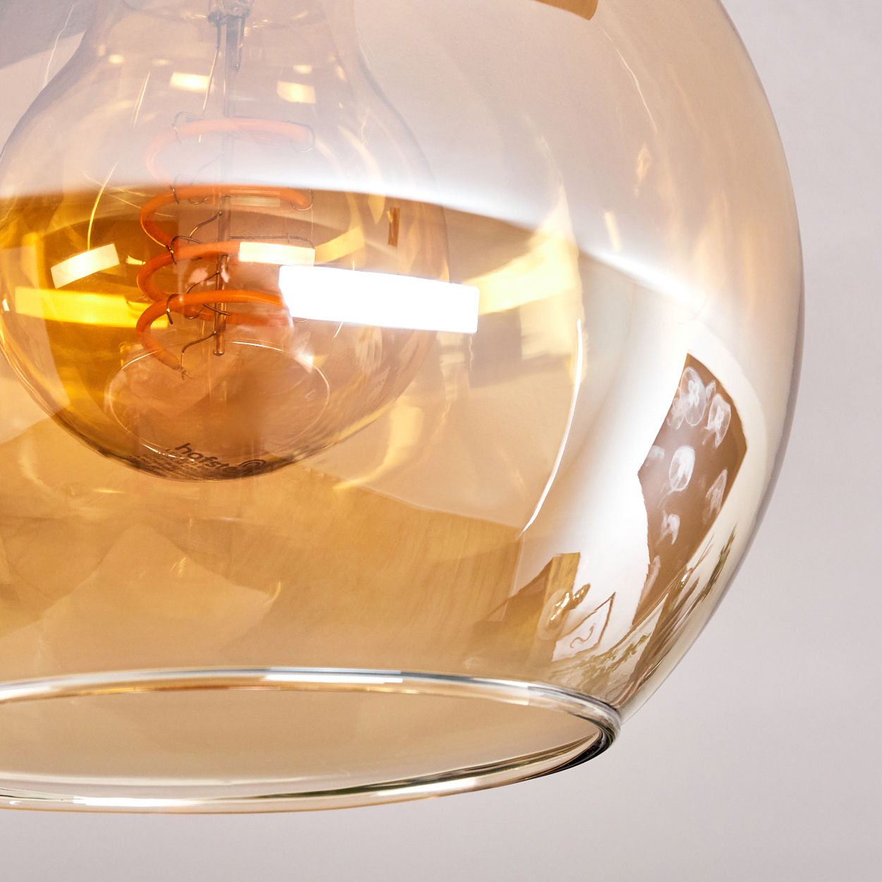 Nahaufnahme einer Glühbirne mit sichtbarem orangefarbenem Glühfaden. Das Glas ist bernsteinfarben und reflektiert Licht. Der Hintergrund ist weiß.