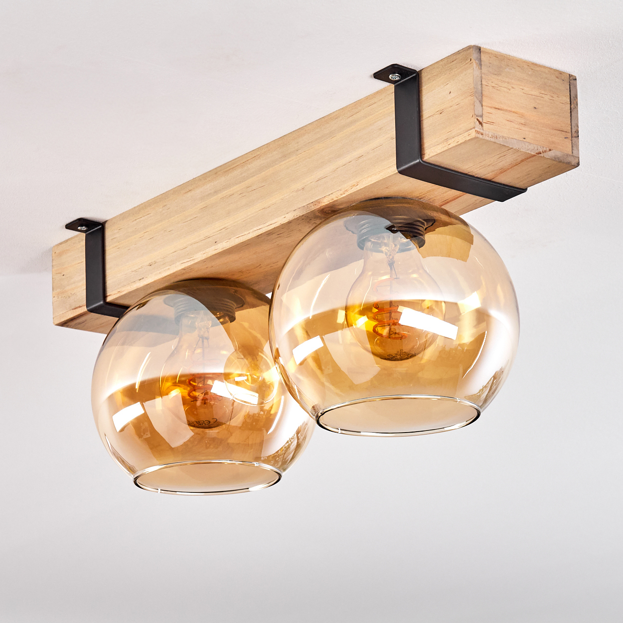 Eine Leuchte mit zwei kugelförmigen Lampen. Die Lampen sind bernsteinfarben. Die Leuchte ist an einem Holzbalken montiert.
