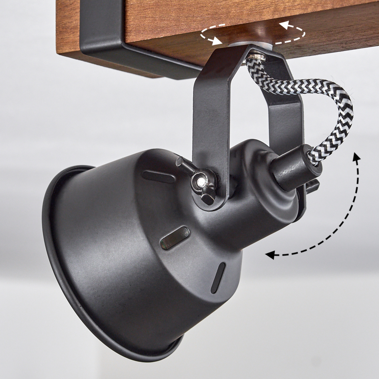 Ein schwarzer Scheinwerfer ist an einem Holzbalken befestigt. Der Scheinwerfer ist verstellbar, mit einem schwarz-weiß geflochtenen Kabel.