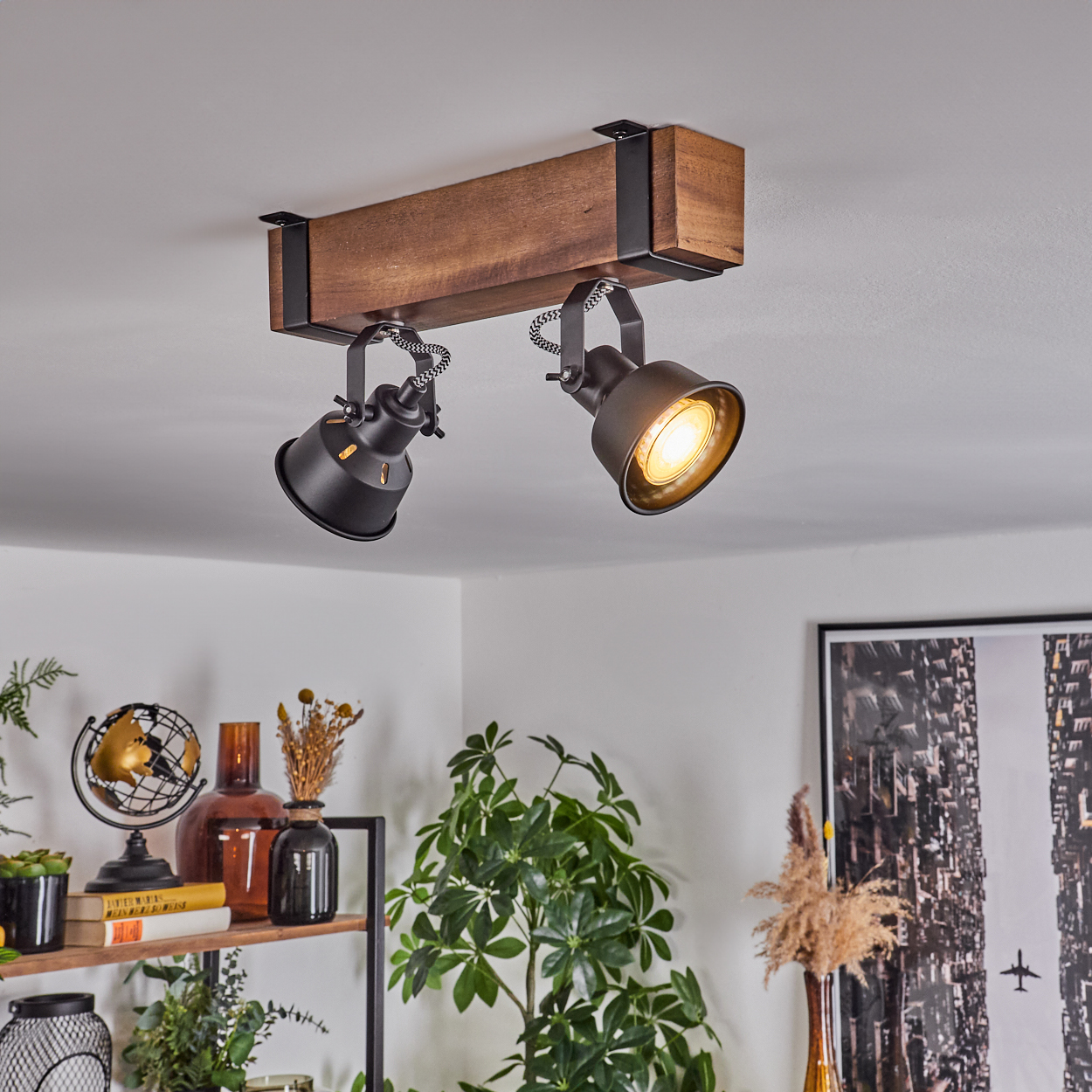 An der Decke montierte Strahler mit zwei schwarzen Lampen an einem Holzbalken. Darunter ist ein Regal mit Pflanzen und Dekoration zu sehen.