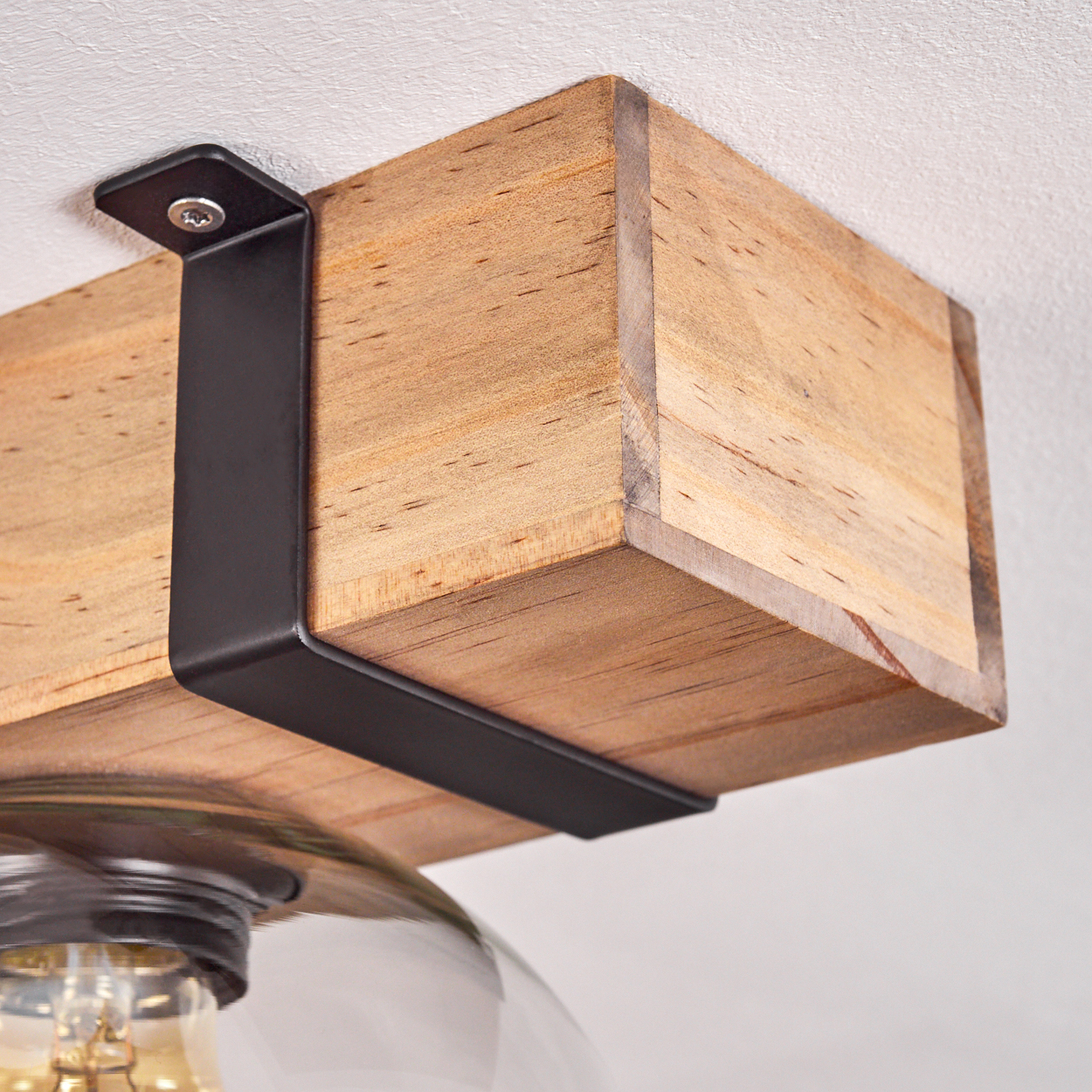 Nahaufnahme eines Holzbalkens, der von einer schwarzen Metallhalterung gehalten wird, die an einer weißen Decke befestigt ist.