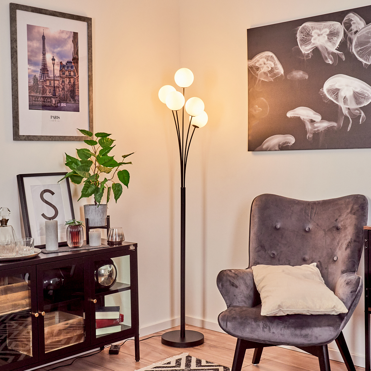 Wohnzimmerszene. Stehlampe, grauer Sessel und schwarzer Schrank mit Kunst. Ein Bild von Paris an der Wand.