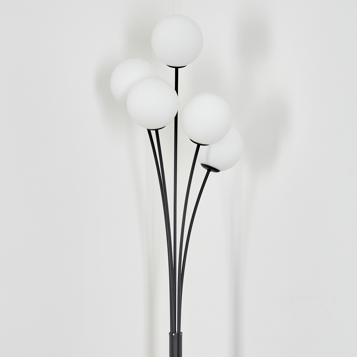 Eine moderne Stehlampe mit fünf weißen Kugelleuchten an schwarzen Stielen. Die Lampe steht vor einer weißen Wand.