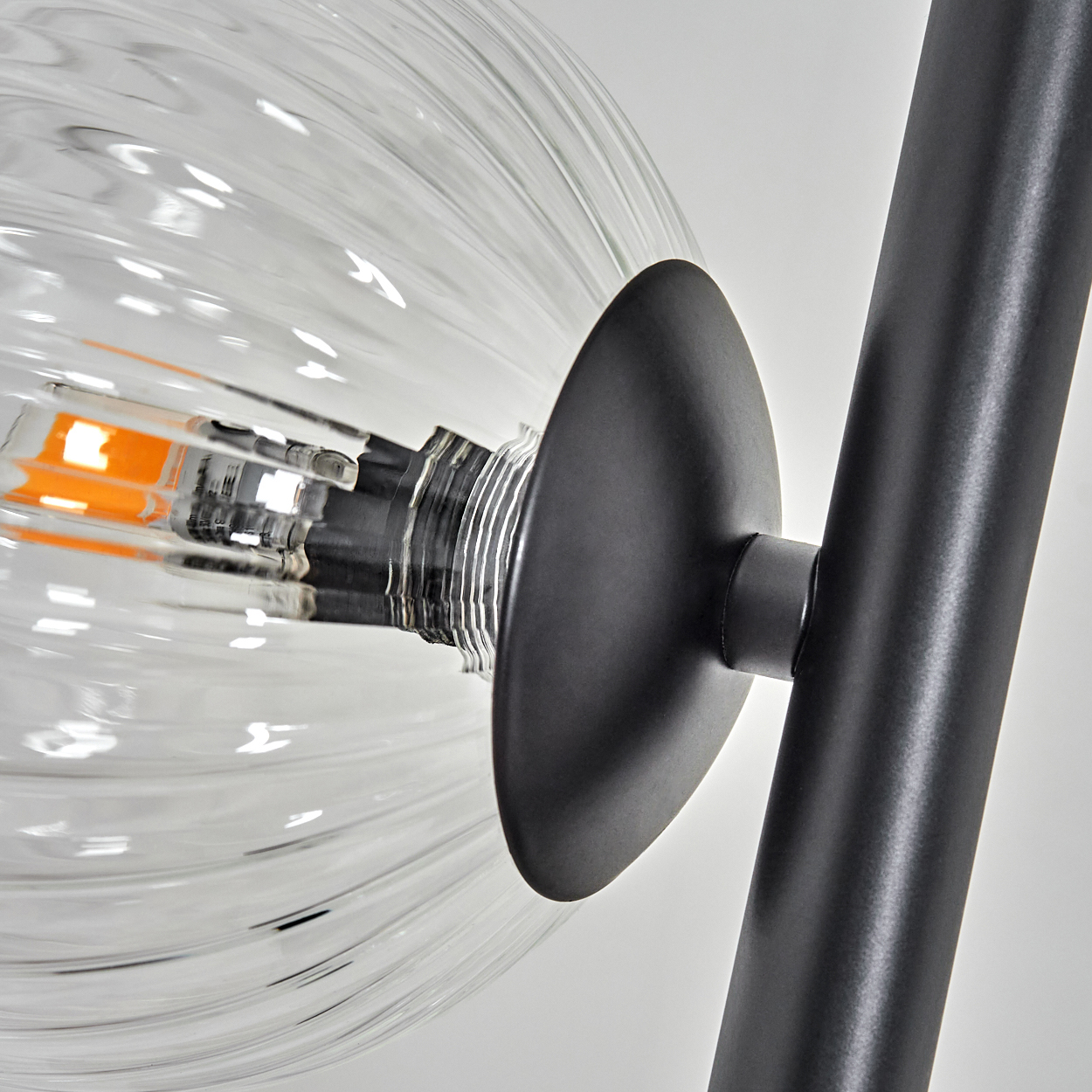 Nahaufnahme einer modernen Lampe. Die Lampe hat einen klaren, gerippten Glaskolben, einen schwarzen Metallsockel und -stiel und ein orangefarbenes Licht.