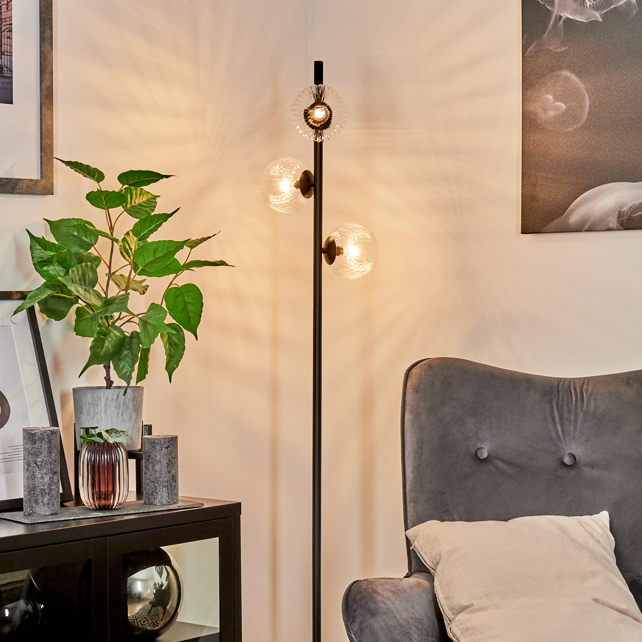 Ein modernes Wohnzimmer mit Stehlampe, grüner Pflanze, Kerzen, grauem Sessel und Gemälde an der Wand.