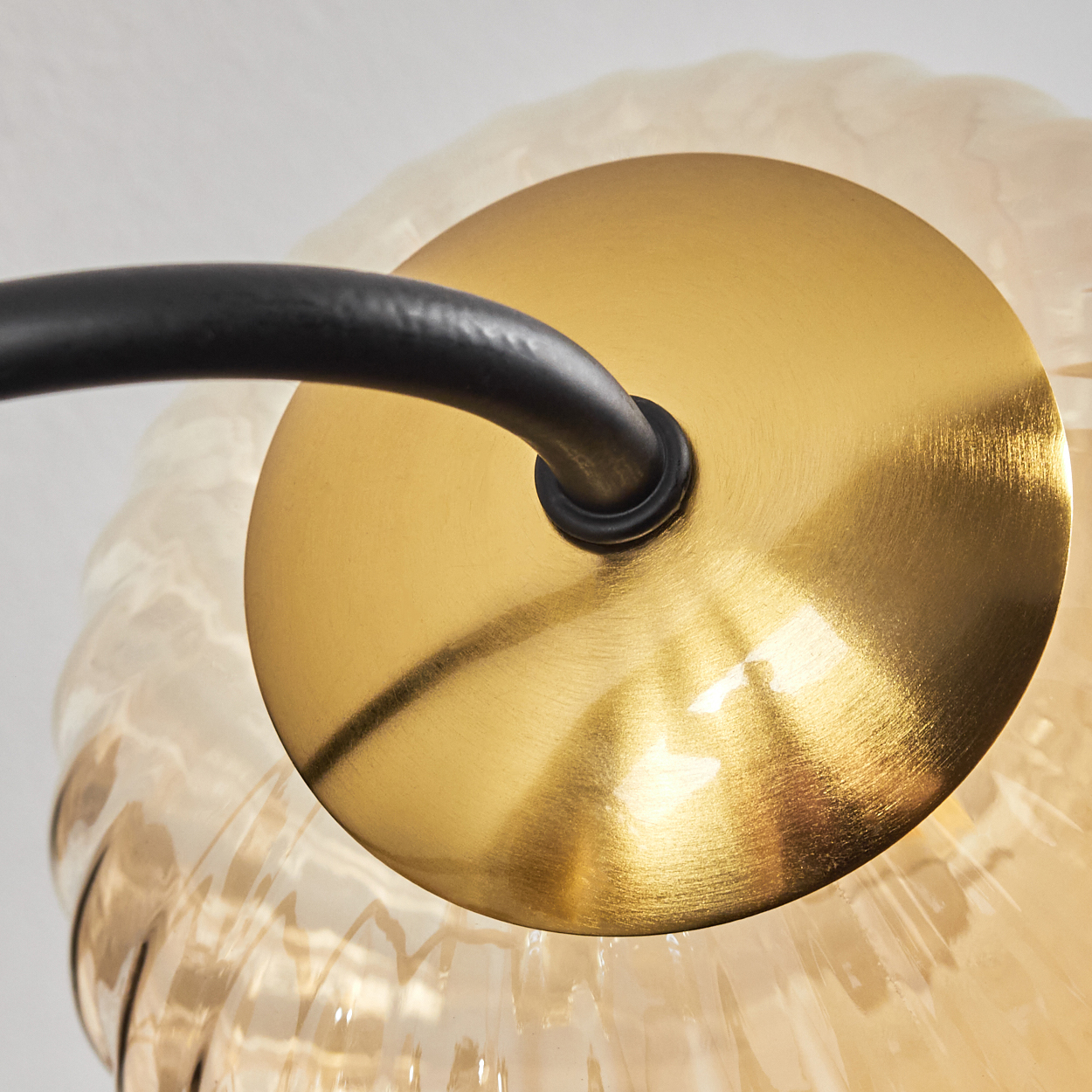 Nahaufnahme einer Lampe. Sie hat eine Messingscheibe, einen schwarzen gebogenen Arm und einen strukturierten Glasschirm.