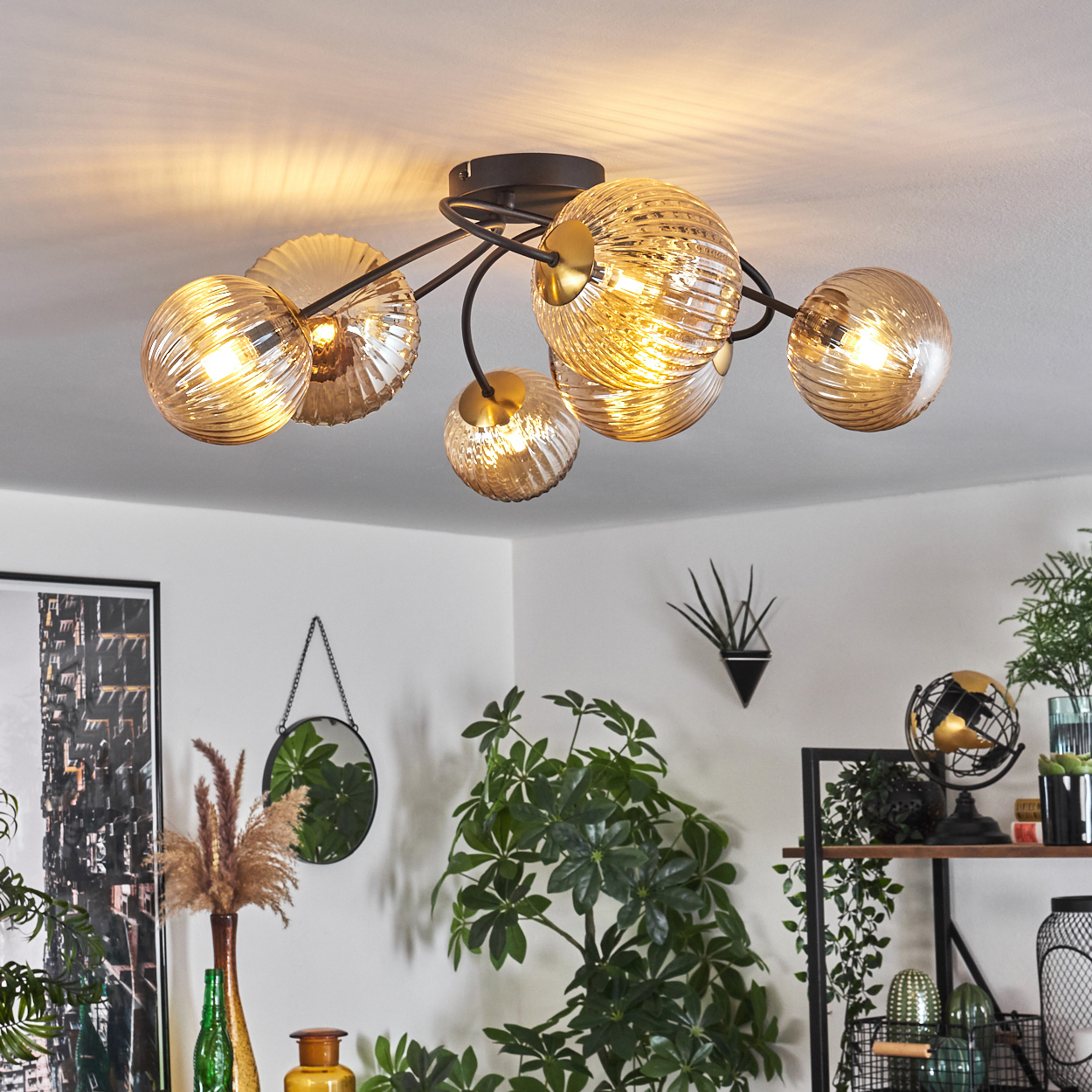 Deckenlampe mit Glaskugeln. Pflanzen und Dekorationen befinden sich an den Seiten. Die Lampe ist gold und schwarz. Weiße Wände und Decke.