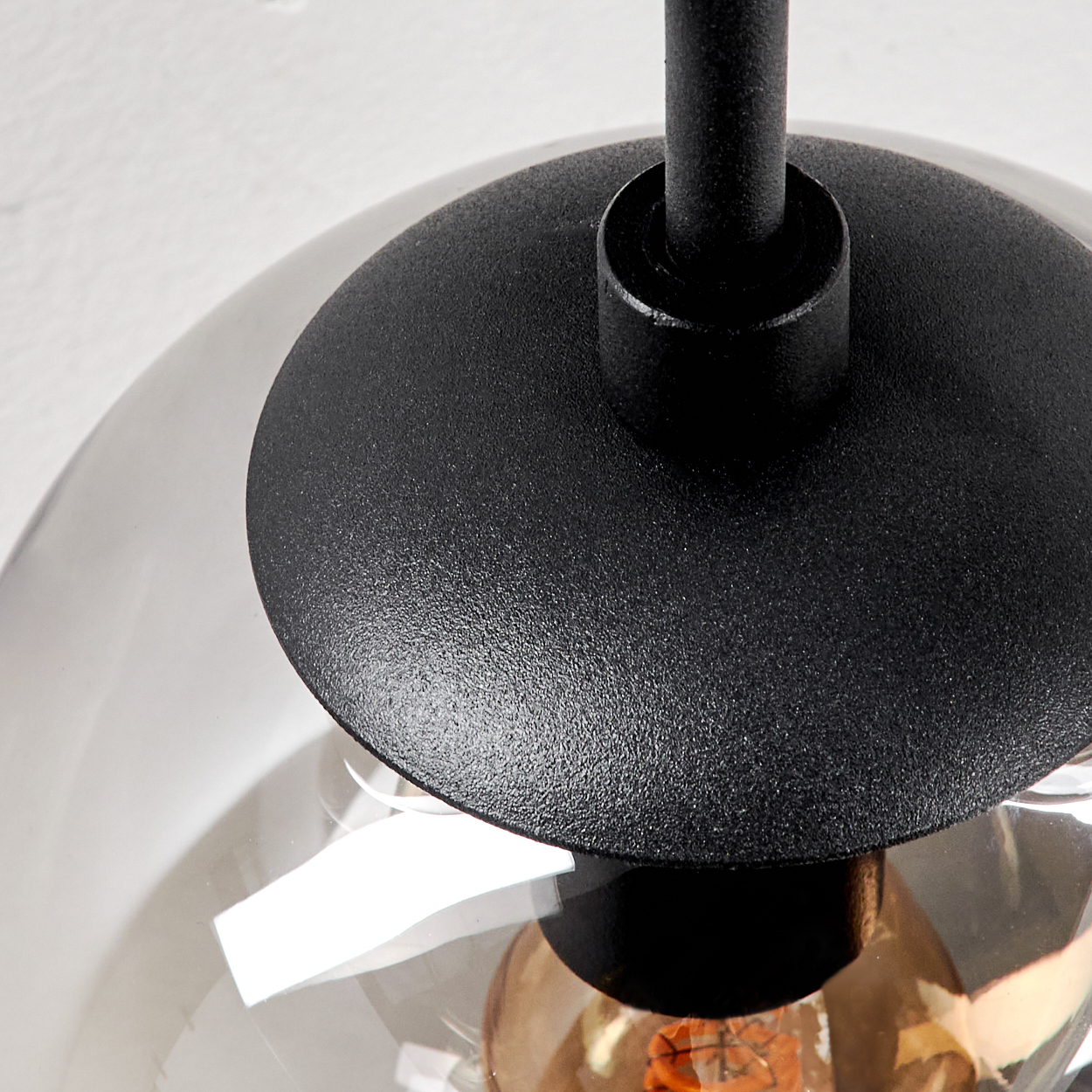 Nahaufnahme eines schwarzen Metall-Lampenschirms mit rundem Glasschirm und sichtbarer Glühbirne. Der Hintergrund ist eine weiße Oberfläche.