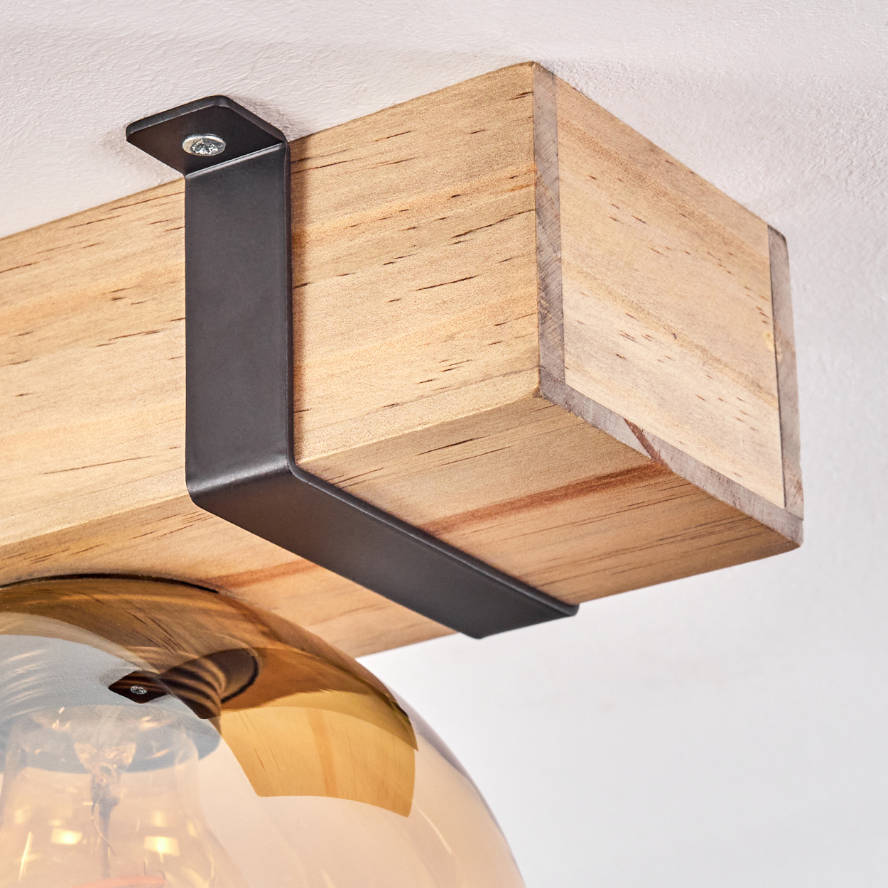 Nahaufnahme eines Holzbalkens mit schwarzen Metallhalterungen und einer gläsernen Leuchte mit goldenem Farbton.