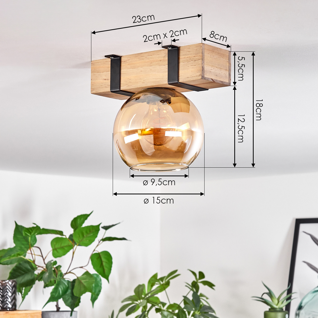 Eine Deckenlampe aus Holz mit kugelförmigem bernsteinfarbenem Glasschirm. Maße sind angegeben. Grüne Pflanzen sind im Vordergrund zu sehen.