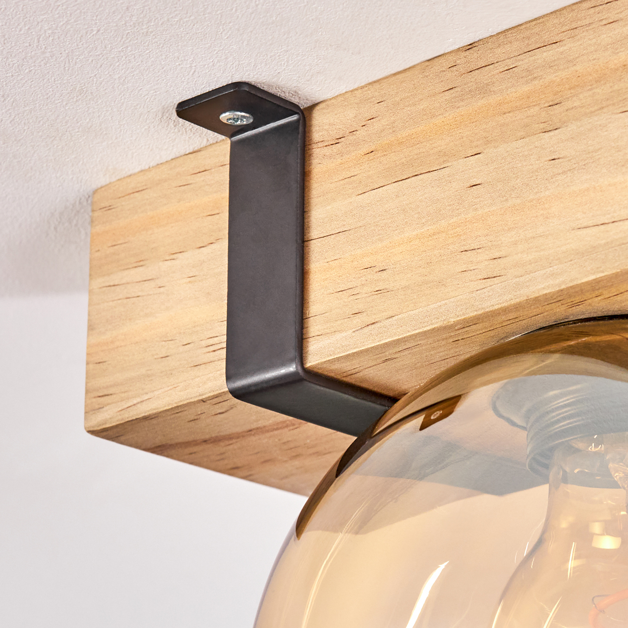 Nahaufnahme eines Holzbalkens mit einer schwarzen Metallhalterung. Eine Leuchte mit Glasschirm ist sichtbar.