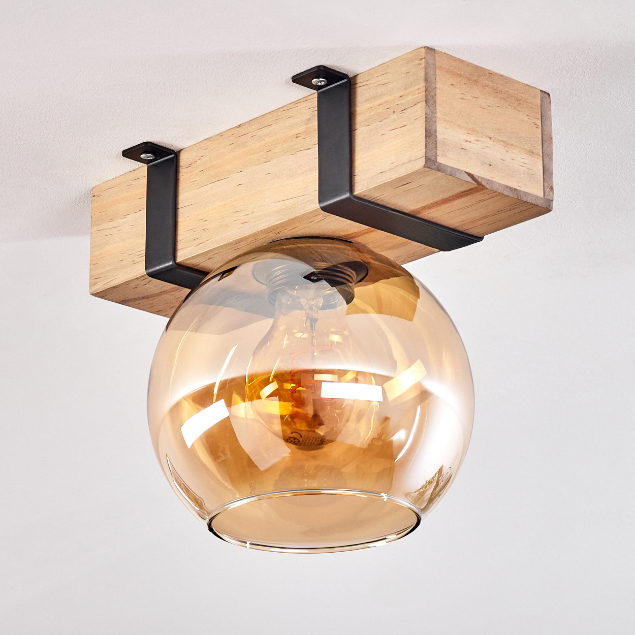 Eine Deckenleuchte mit Holzbalken, schwarzen Metallstützen und einem kugelförmigen Schirm aus bernsteinfarbenem Glas.