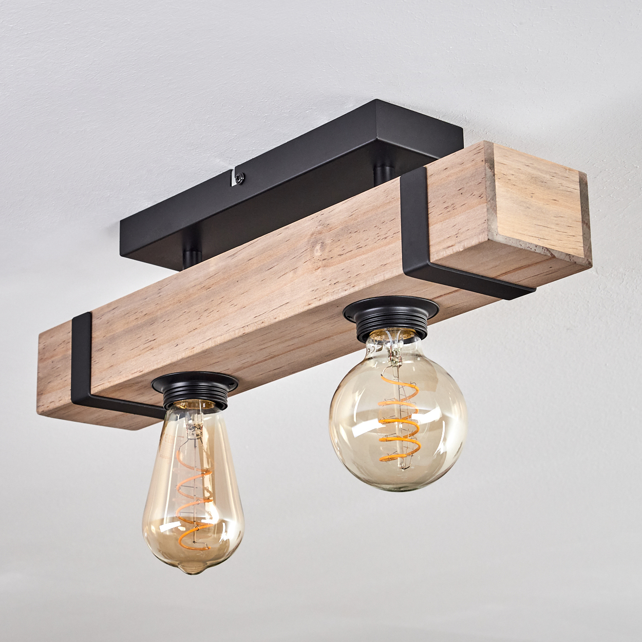 Deckenleuchte. Ein Holzbalken mit zwei Glühbirnen, getragen von schwarzen Metallwinkeln, an einer schwarzen Basis befestigt.