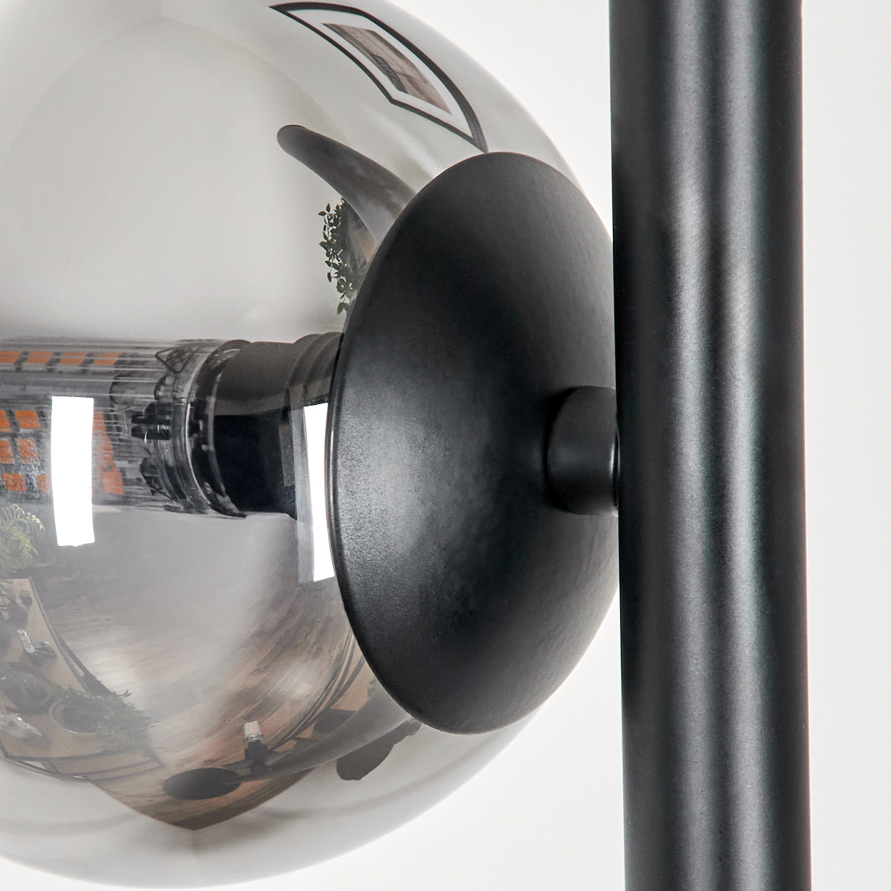 Nahaufnahme einer schwarzen Lampe. Eine transparente Kugel reflektiert die Umgebung. Eine schwarze Scheibe und ein Pfosten sind ebenfalls sichtbar.