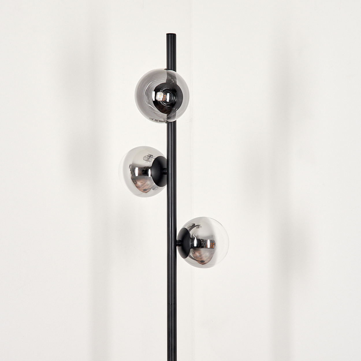 Eine schwarze Metall-Stehlampe mit drei kugelförmigen Glasschirmen. Die Schirme sind reflektierend, der Hintergrund ist eine weiße Wand.