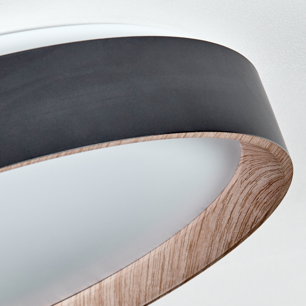 Nahaufnahme einer modernen Lampe mit schwarzem Oberteil, Holzsockel und weißem Innenraum. Die Lampe steht vor weißem Hintergrund.