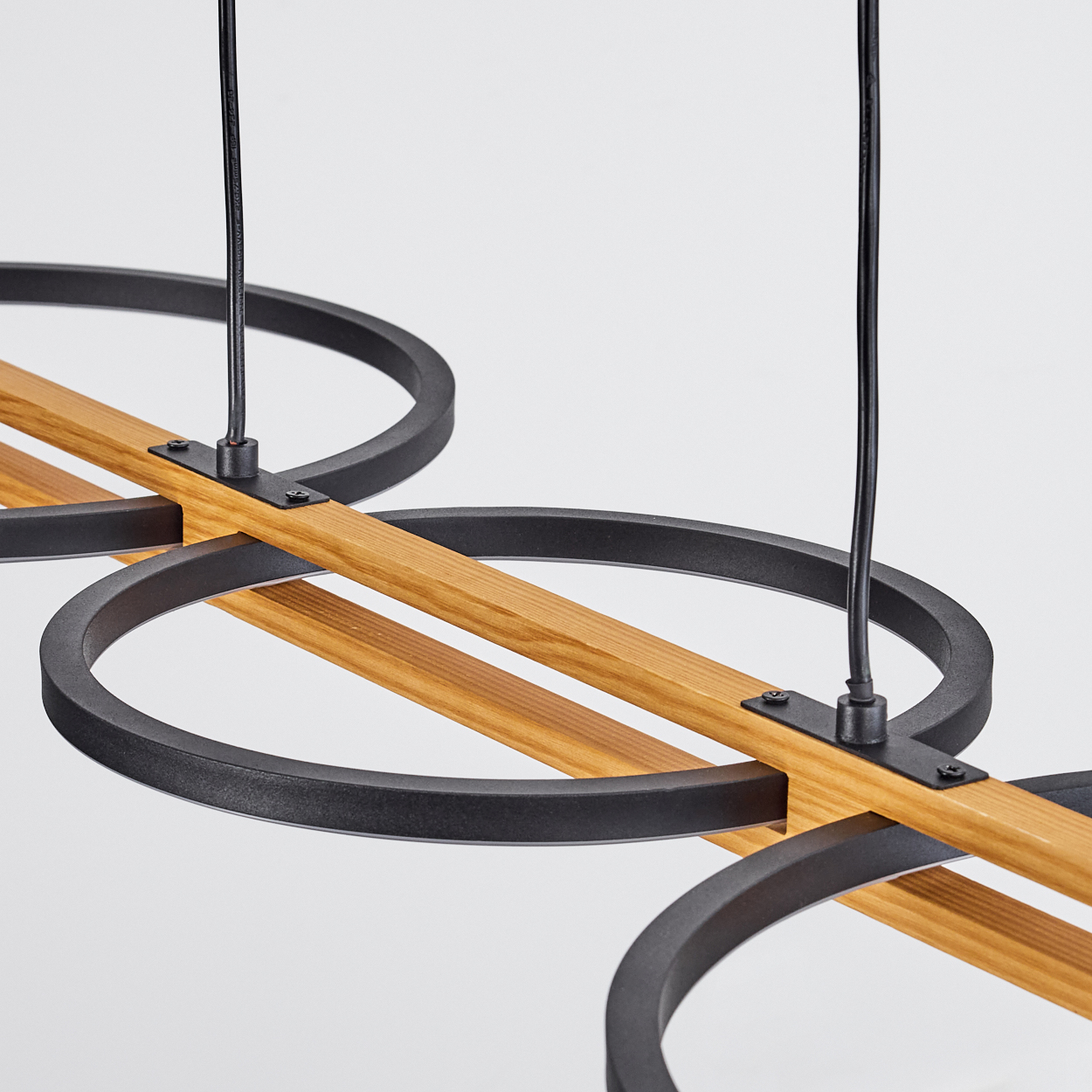 Nahaufnahme einer modernen Leuchte. Sie hat schwarze Metallringe, Holzbalken und schwarze Kabel vor weißem Hintergrund.
