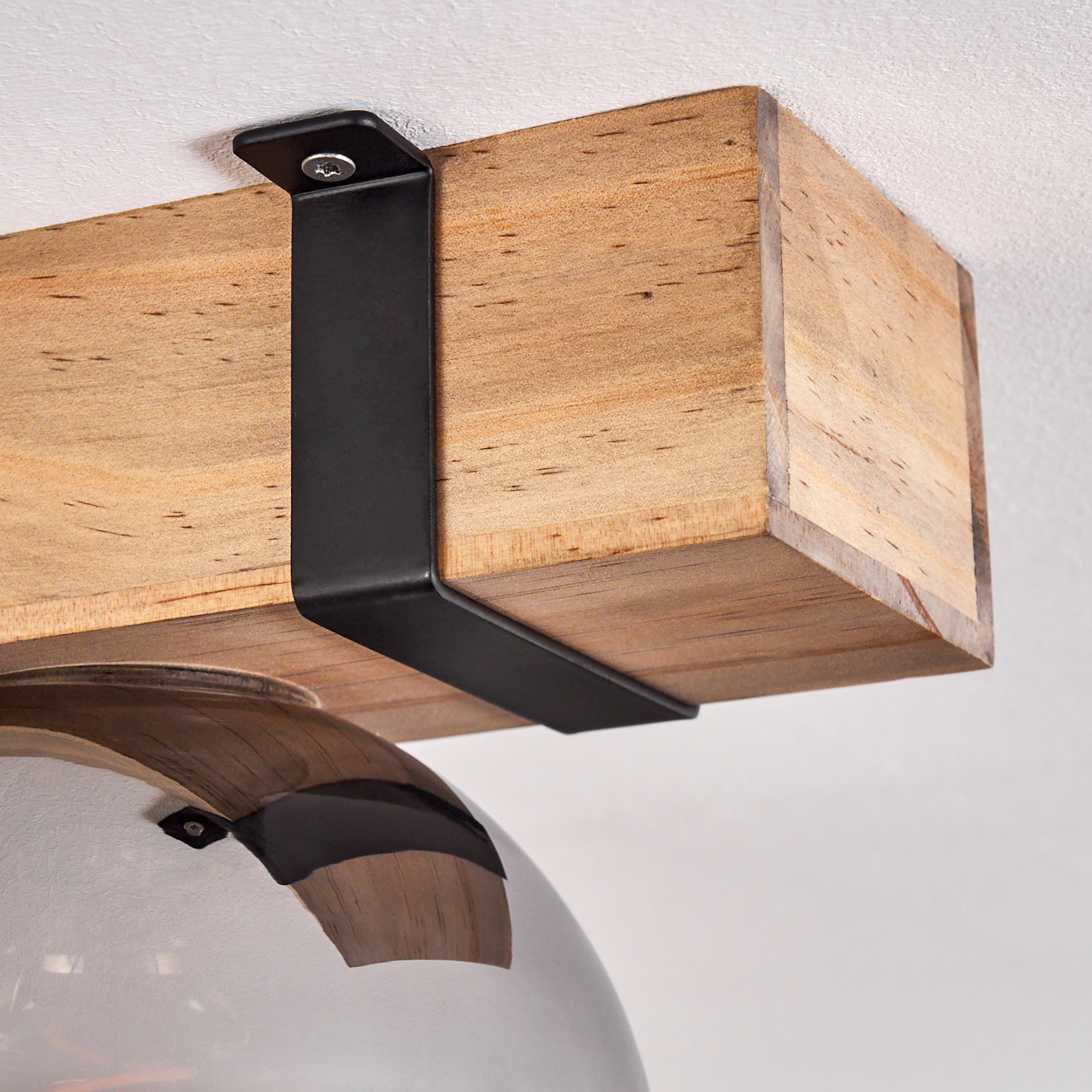 Ein Holzbalken, der von einer schwarzen Metallhalterung gehalten wird. Darunter ein Glasschirm. Die Decke ist weiß.