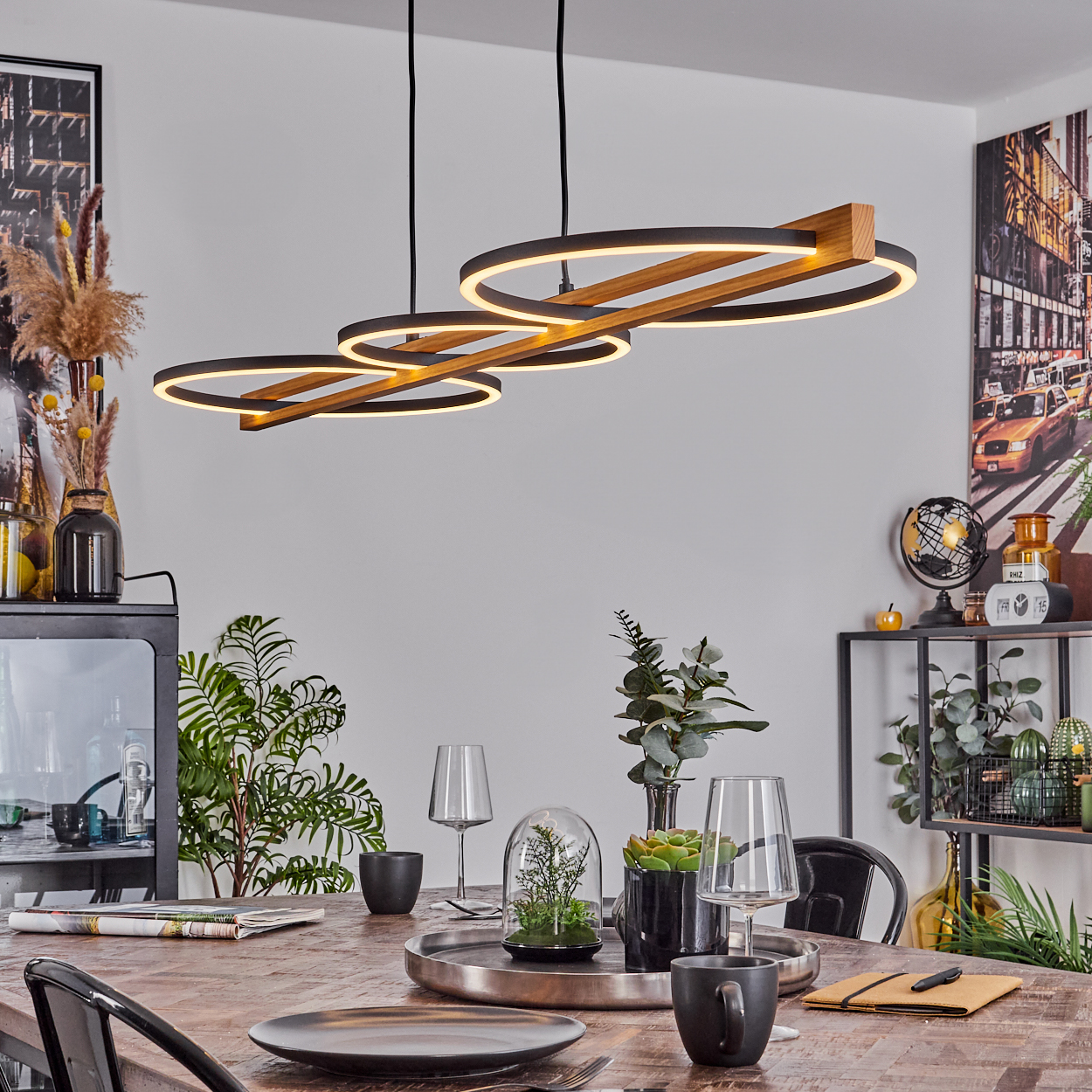 Esszimmer mit Holztisch, schwarzen Stühlen. Moderne Hängelampe mit drei Lichtringen. Dekorationen und Kunst an den Wänden.