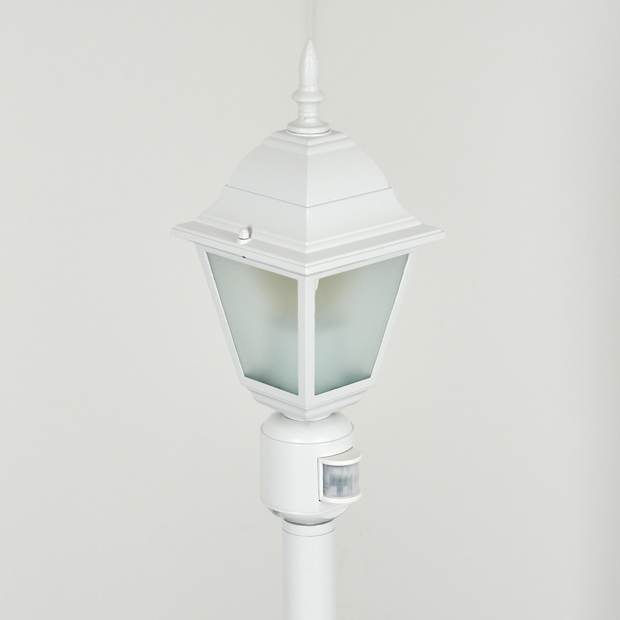 Eine weiße Außenlampe mit Bewegungssensor vor schlichtem, weißem Hintergrund. Die Lampe hat ein klassisches Design.