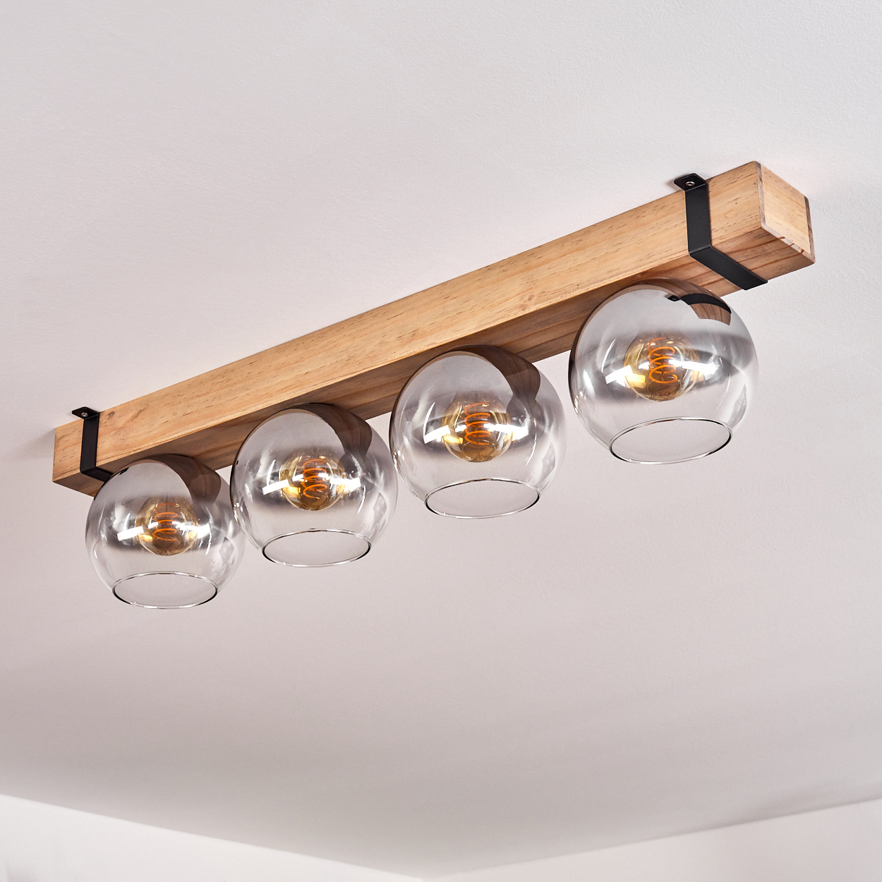 Deckenleuchte mit vier Glaskugelschirmen, befestigt an einem Holzbalken, der von der weißen Decke abgehängt ist.