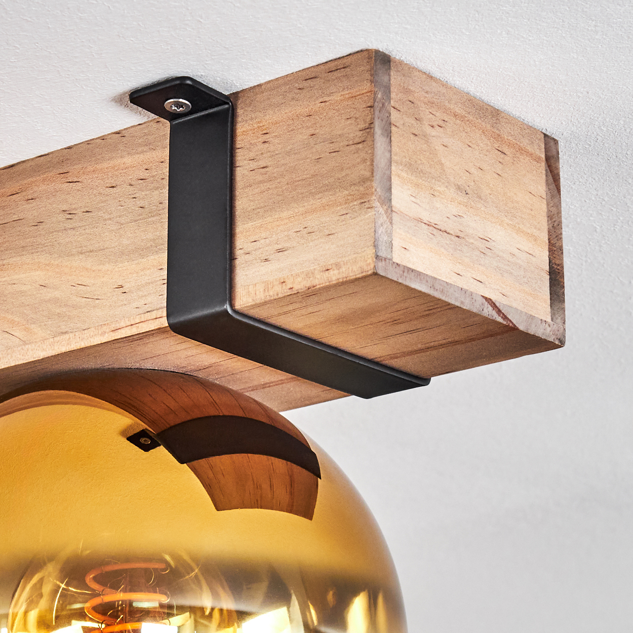 Eine Leuchte mit Holzbalken, schwarzem Metallbügel und einer goldenen Glaskugel. Der Glühfaden der Glühbirne ist sichtbar.