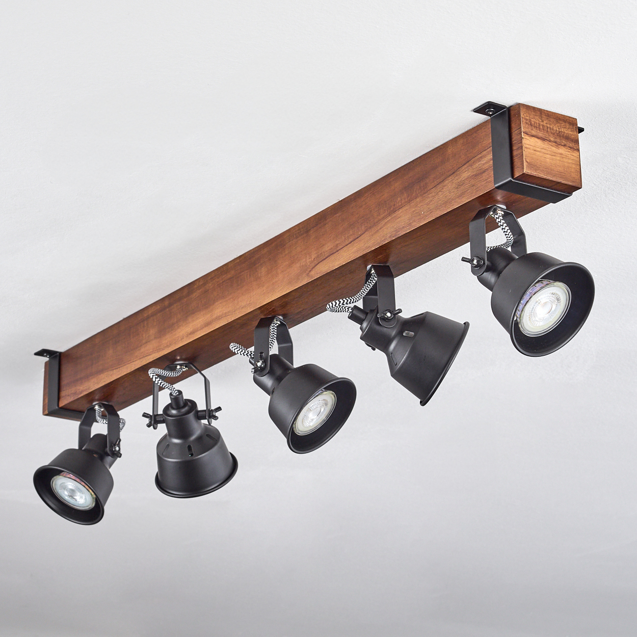 Eine Deckenstrahler-Leuchte mit fünf schwarzen Lampen, die an einem Holzbalken befestigt sind. Die Lampen haben weiß-schwarz gestreifte Kabel.