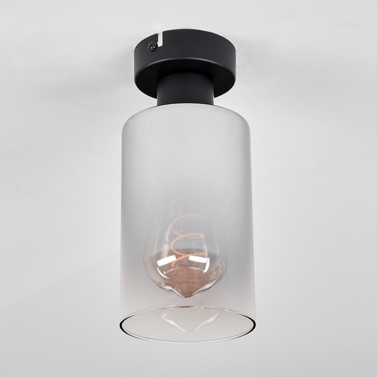 Eine Deckenleuchte mit schwarzem Sockel und mattiertem Glasschirm. Die Glühbirne hat einen sichtbaren orangefarbenen Glühfaden.