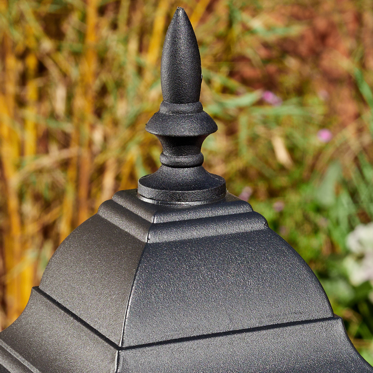 Nahaufnahme einer schwarzen, verzierten Metallstruktur mit spitzer Spitze. Der Hintergrund ist verschwommenes grünes und braunes Laub.