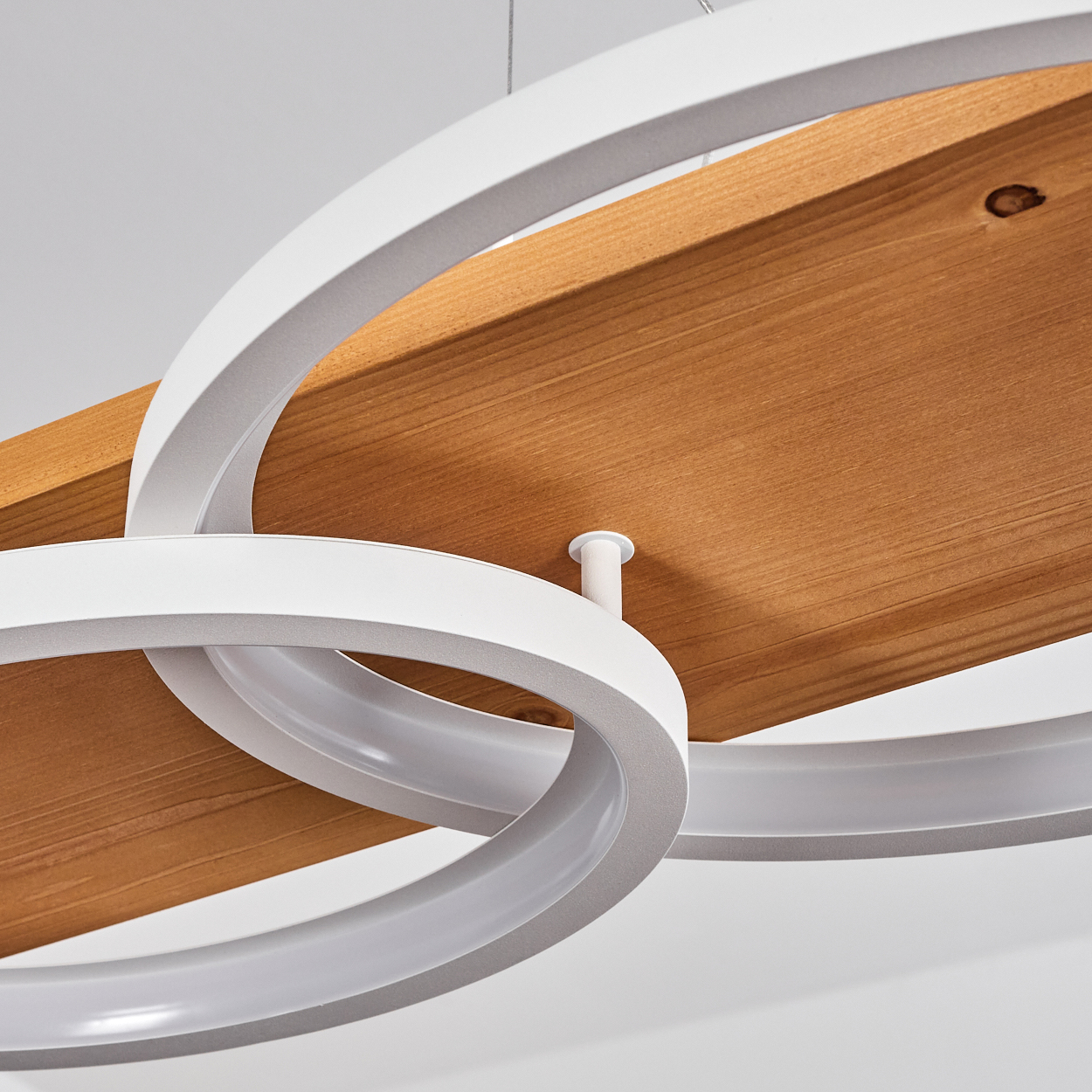 Moderne Hängelampe mit weißen, gebogenen Ringen und einer Holzplanke. Der Hintergrund ist weiß. Die Ringe überlappen die Holzplanke.
