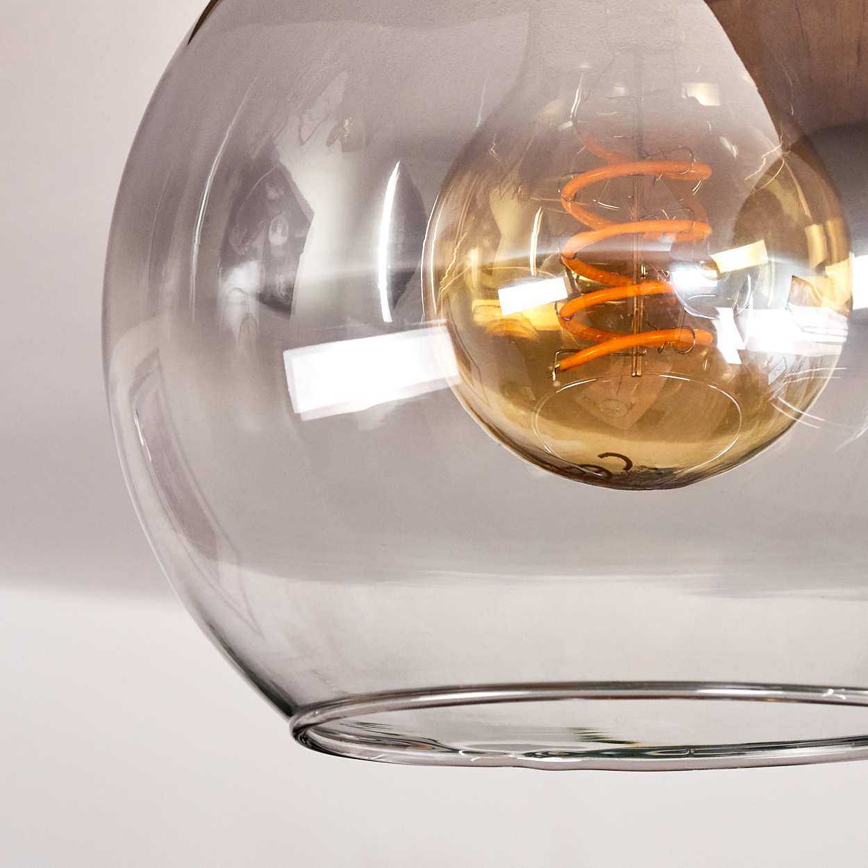 Ein klarer Glasschirm umgibt eine Glühbirne mit einem orangefarbenen Wendelfaden. Der Hintergrund ist eine weiße Wand.