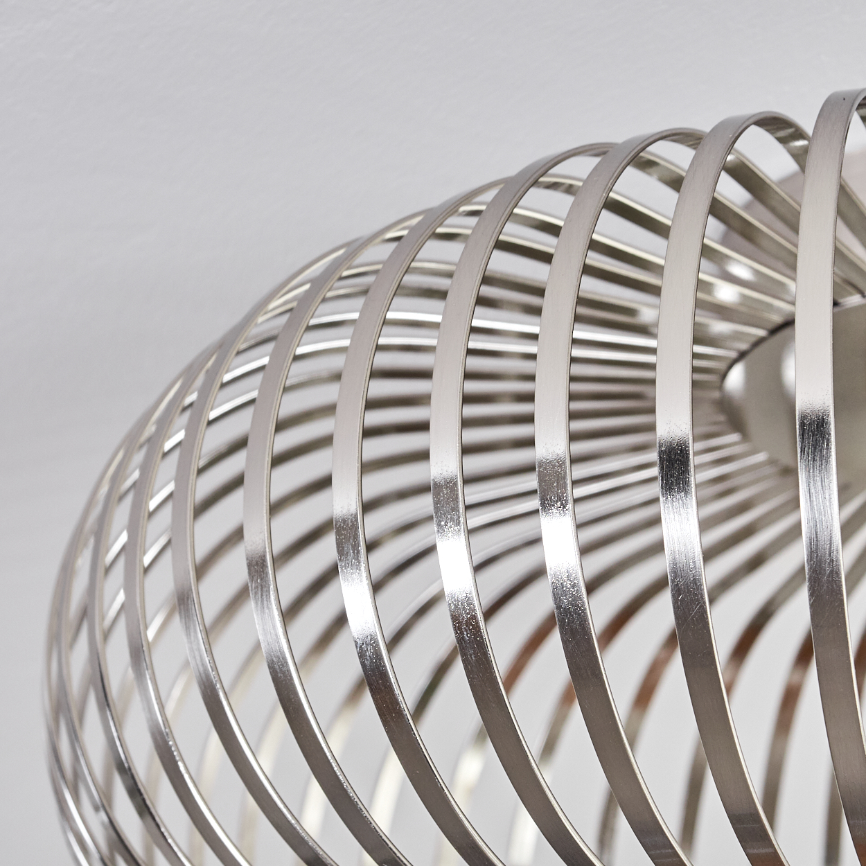 Nahaufnahme einer silbernen, käfigartigen Pendelleuchte. Die Leuchte hat ein spiralförmiges Design mit weißem Hintergrund.
