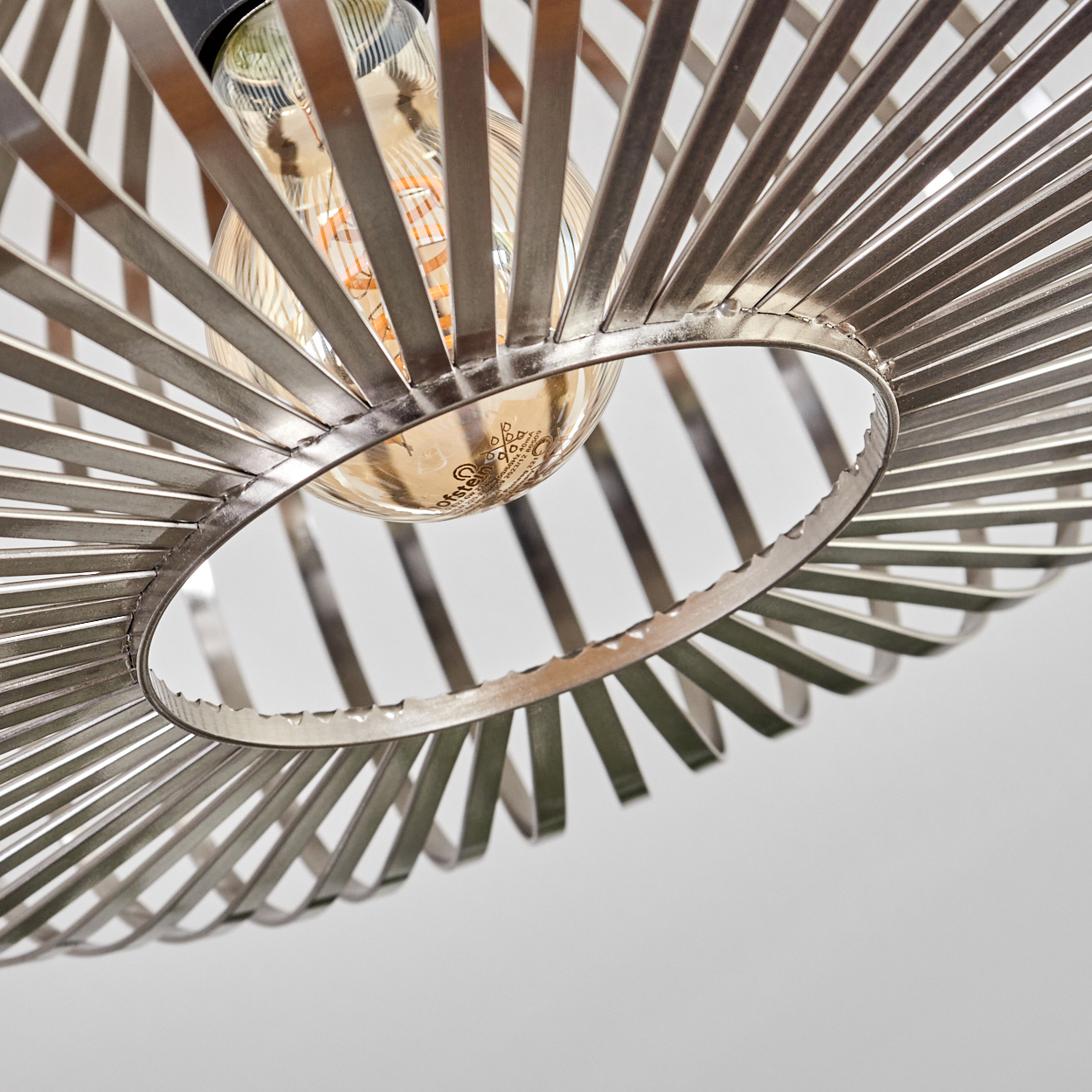 Nahaufnahme einer metallischen Leuchte mit einer Glühbirne. Die Leuchte hat ein kreisförmiges Design mit radialen Metallstreifen. Der Hintergrund ist weiß.