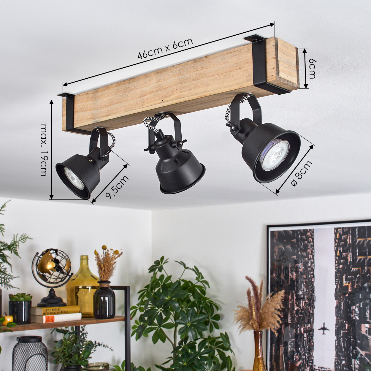 Deckenstrahler mit drei schwarzen Lichtern, die an einem Holzbalken befestigt sind. Abmessungen sind angegeben. Dekorative Regal mit Pflanzen im Hintergrund.