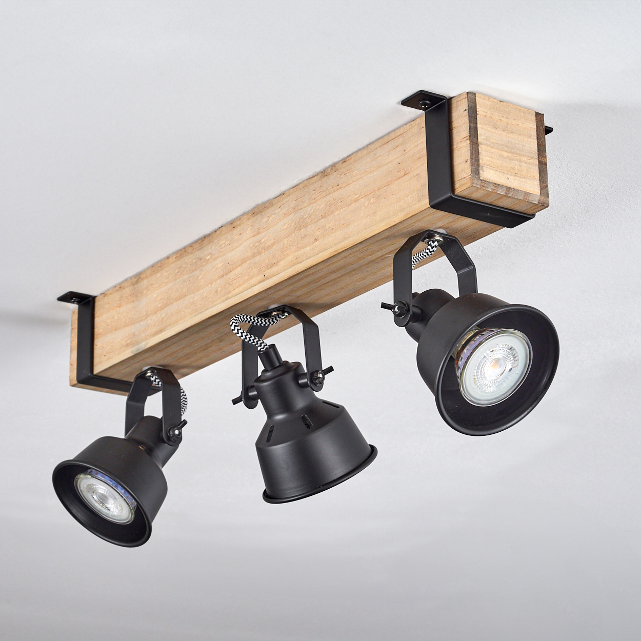 Drei schwarze Strahler an einem Holzbalken befestigt. Der Balken ist an der Decke befestigt. Der Hintergrund ist weiß.