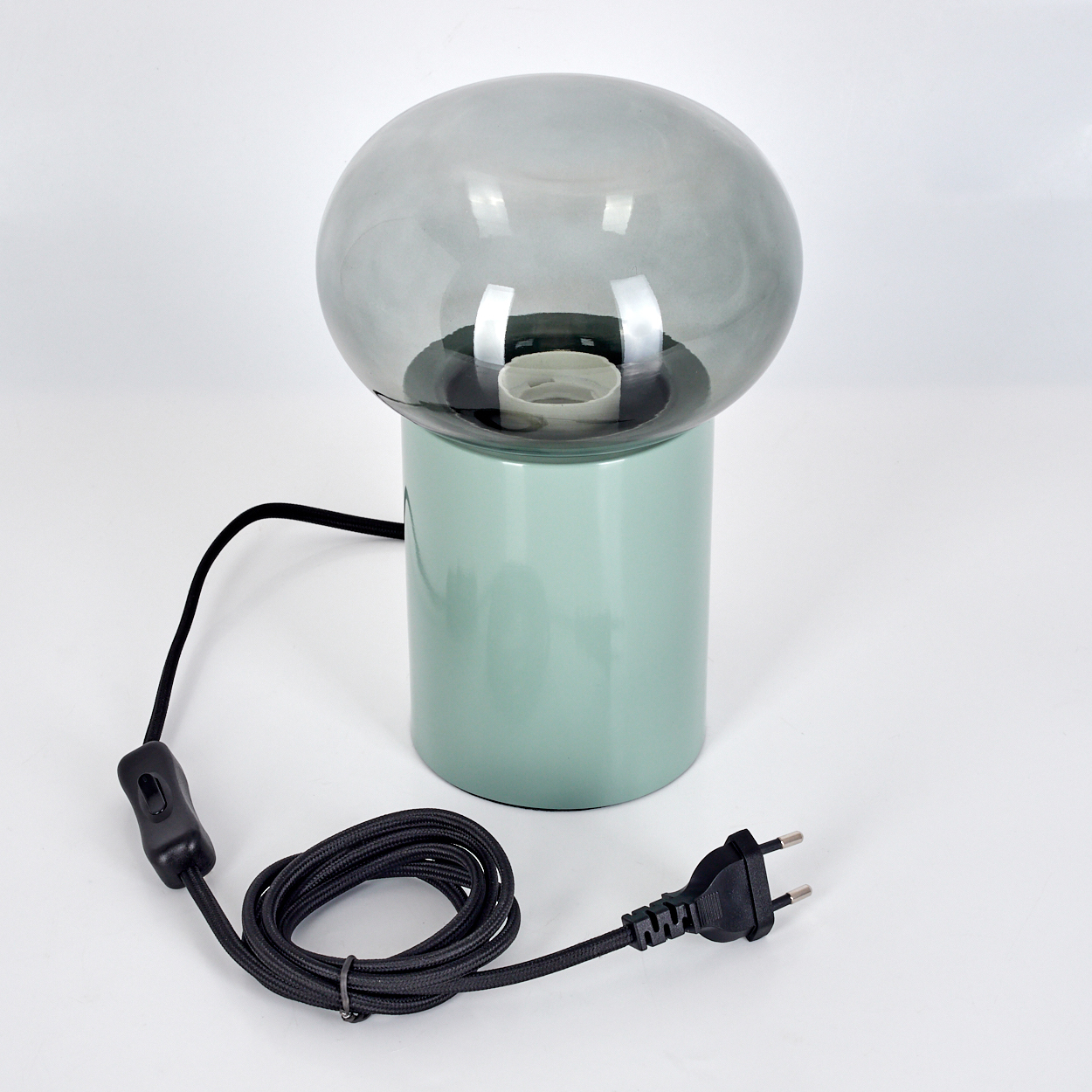 Eine pilzförmige Lampe mit grauem Glasschirm, hellgrüner Basis und schwarzem Kabel mit Schalter und Stecker auf weißem Hintergrund.