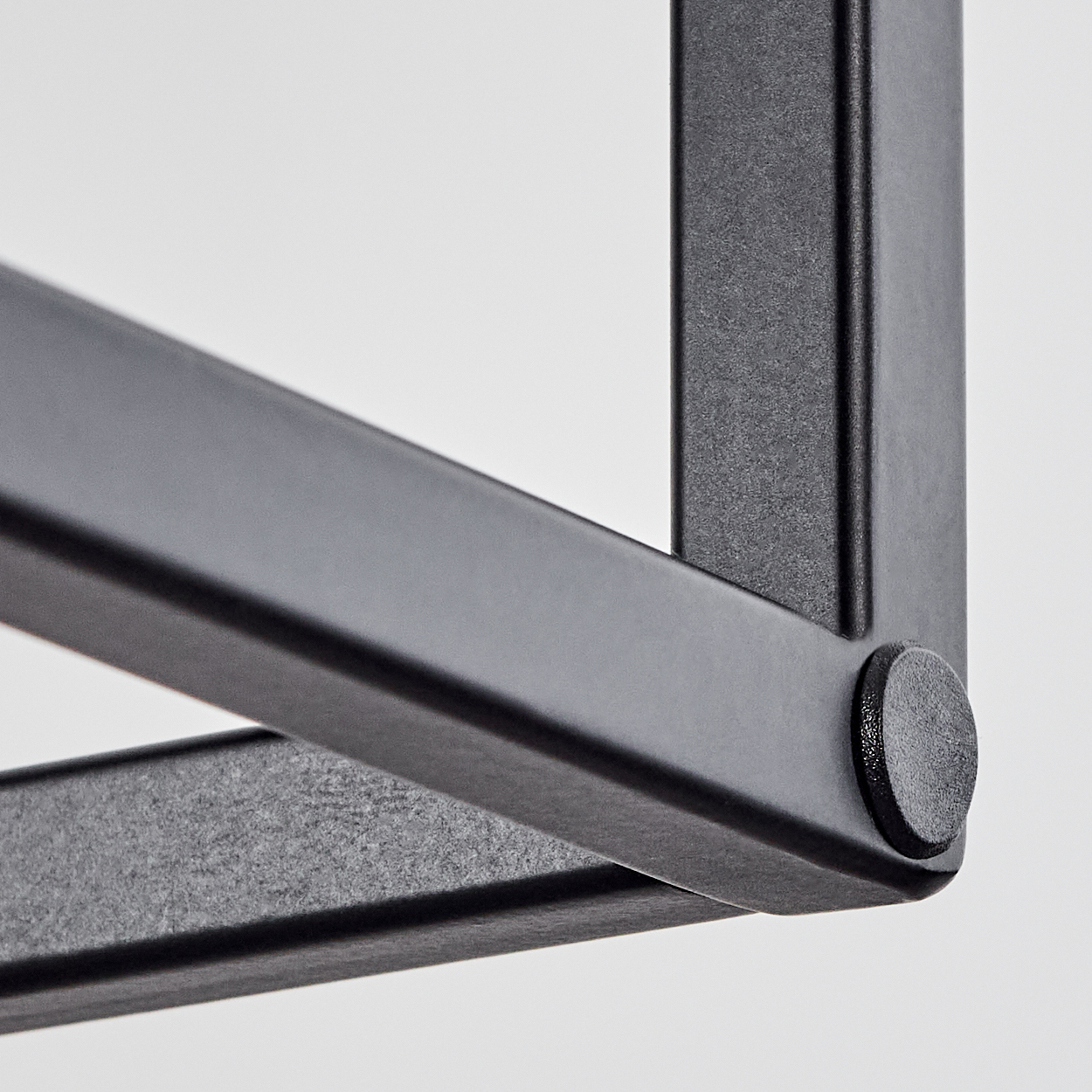 Nahaufnahme einer schwarzen Metalleckkonstruktion vor weißem Hintergrund. Ein kleines, rundes schwarzes Teil verbindet die Balken.