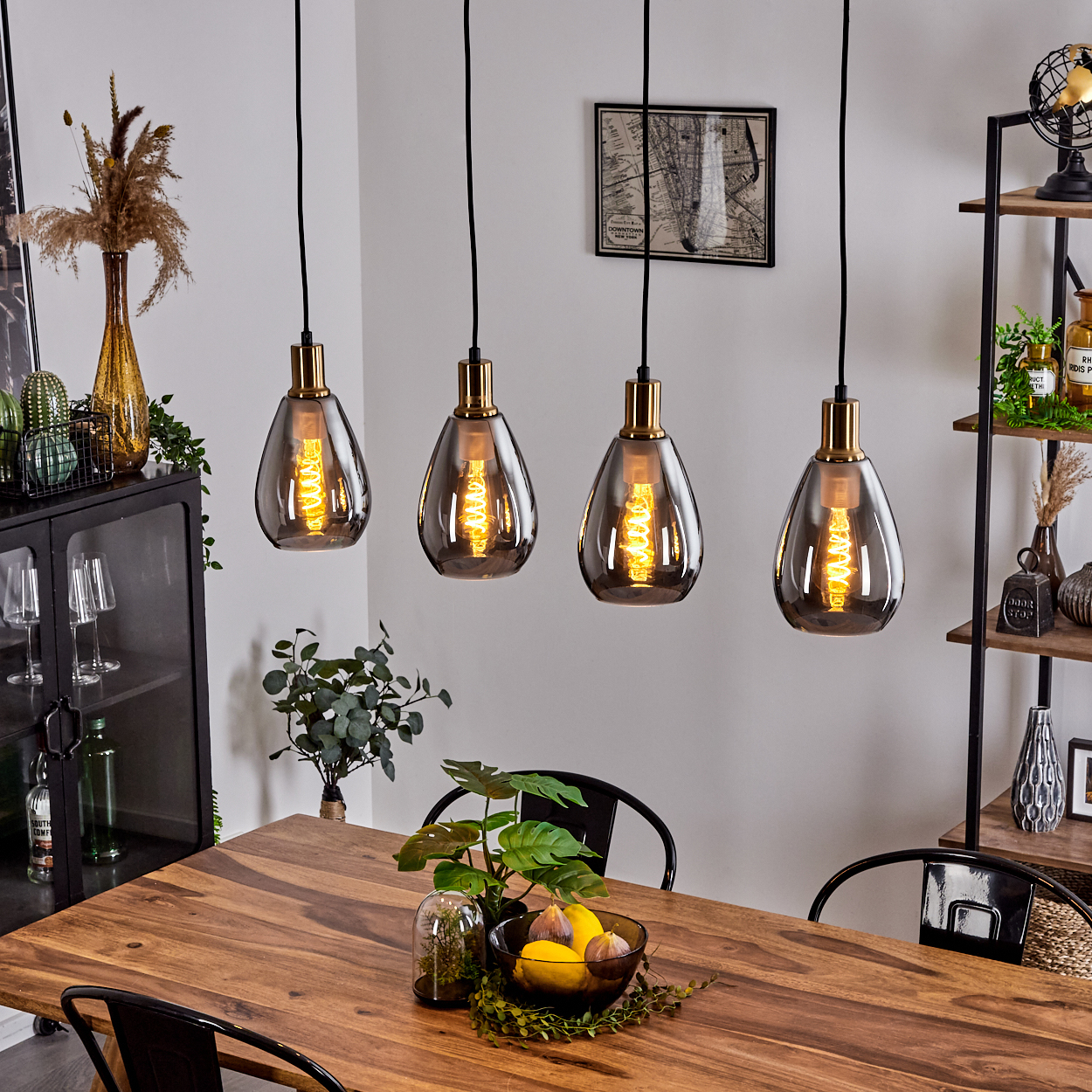 Esszimmer mit Holztisch, vier Hängelampen und Regal mit Deko. Auf dem Tisch steht eine Obstschale.