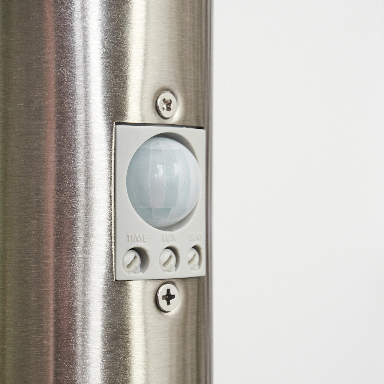 Nahaufnahme eines silbernen Metallzylinders mit einem Sensorfeld. Das Feld hat einen Bewegungssensor und Einstellräder mit den Bezeichnungen TIME, LUX und SENS.