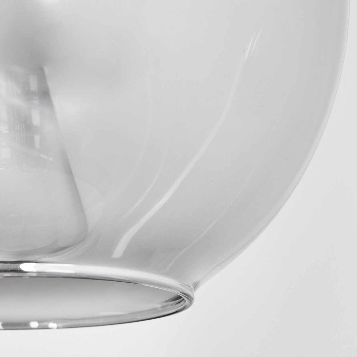 Nahaufnahme eines transparenten Glaslampenschirms. Das Glas ist gebogen und hat eine hellgraue Farbe. Der Hintergrund ist weiß.