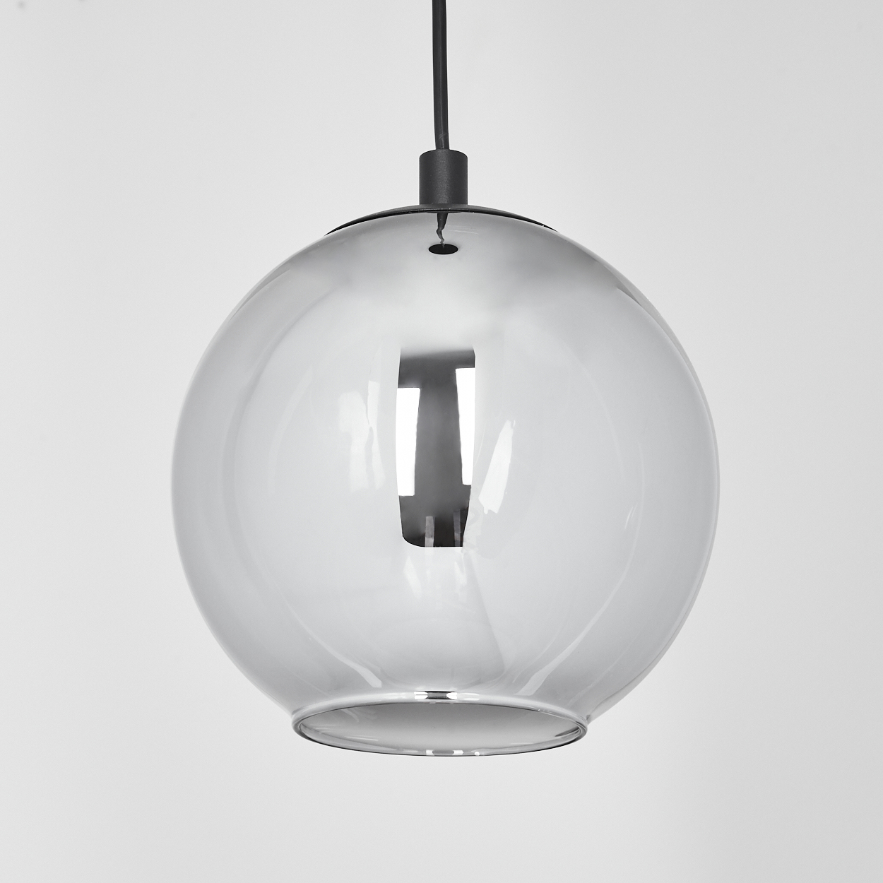 Eine kugelförmige, graue Glas-Pendelleuchte hängt an einem schwarzen Kabel. Das Glas reflektiert Licht und eine dunkle, rechteckige Form.