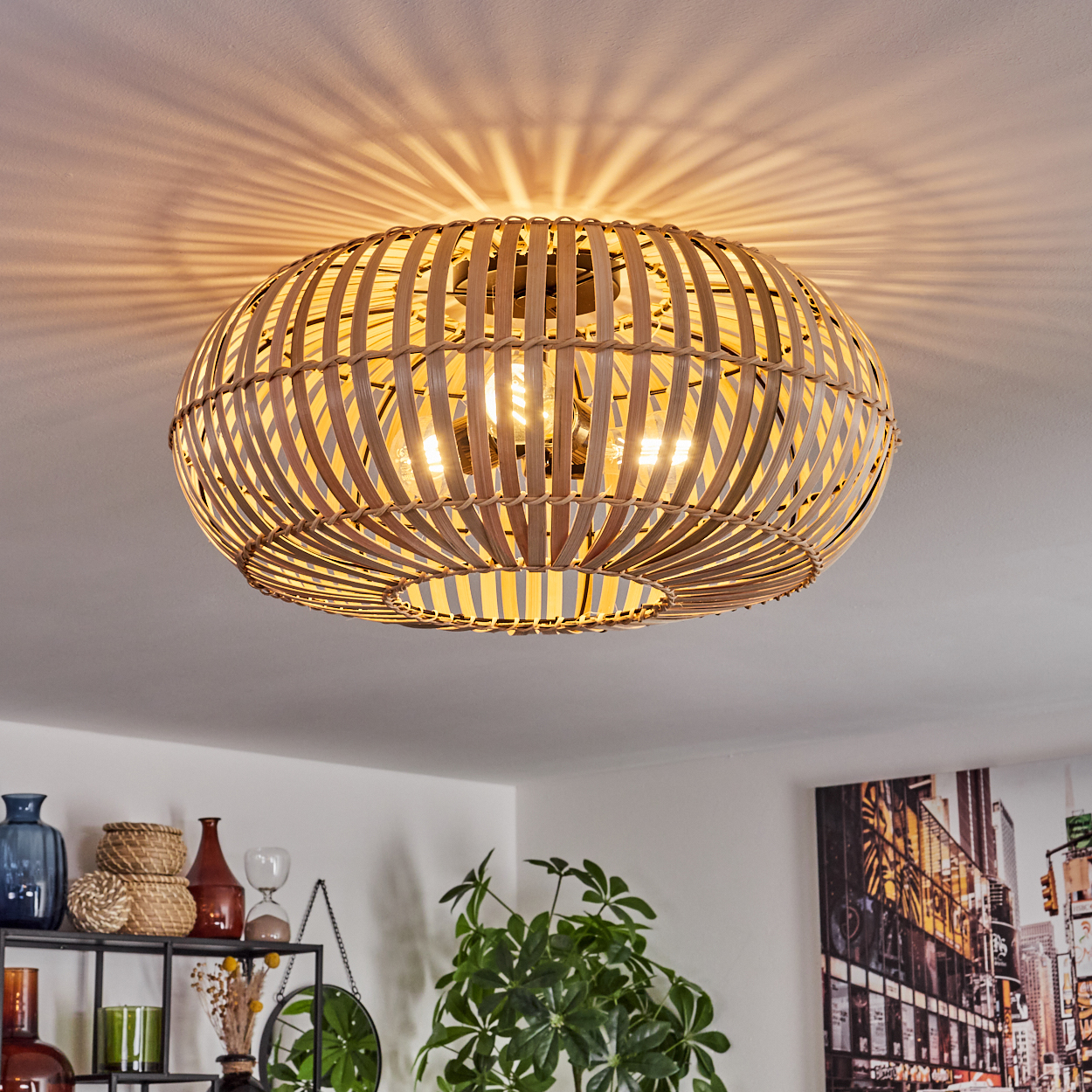 Eine Deckenlampe im Bambus-Stil wirft Licht auf die Decke. Darunter sind ein Regal mit Vasen, Pflanzen und ein Stadtbildgemälde zu sehen.