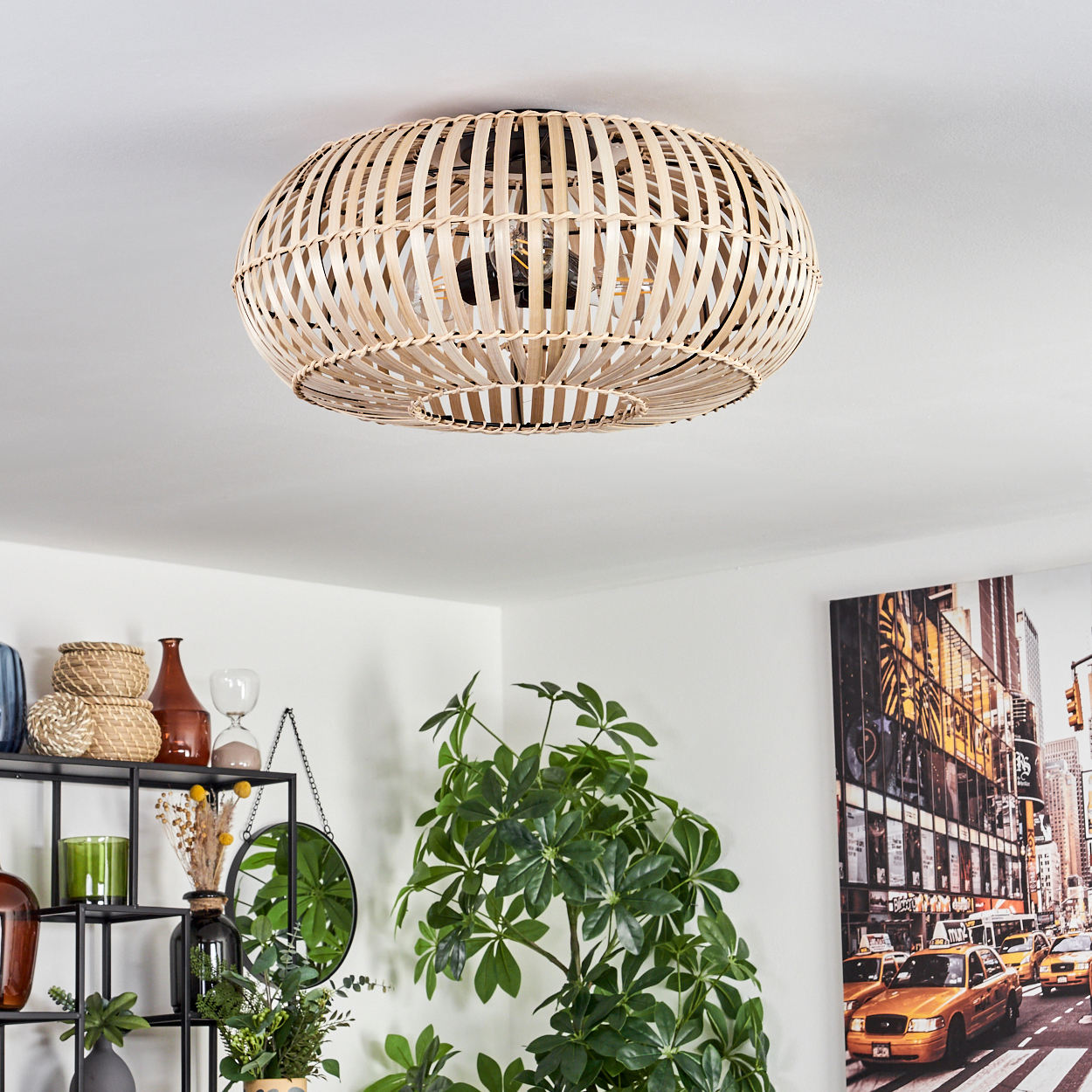 Eine gewebte Deckenlampe aus Rattan. Darunter ist ein Regal mit Dekoration und Pflanzen zu sehen. Ein Stadtbild hängt an der Wand.