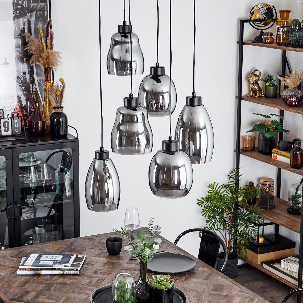 Esszimmer mit hängenden silbernen Lichtern. Tisch mit Dekoration, einem schwarzen Schrank und einem Bücherregal.