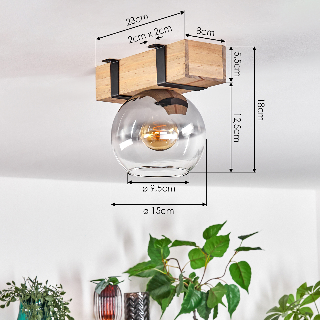 Eine moderne Deckenlampe mit Holzbalken und klarer Glaskugel. Abmessungen sind angegeben. Pflanzen im Hintergrund.