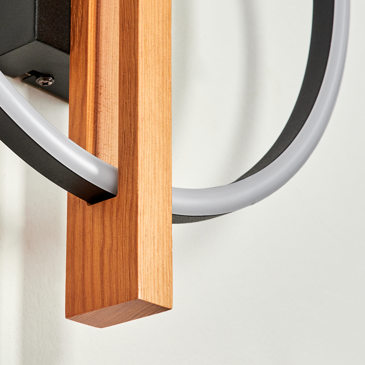 Eine moderne Wandleuchte mit einem Holzblock und einem schwarzen Ring mit weißem, beleuchtetem Teil. Der Hintergrund ist weiß.