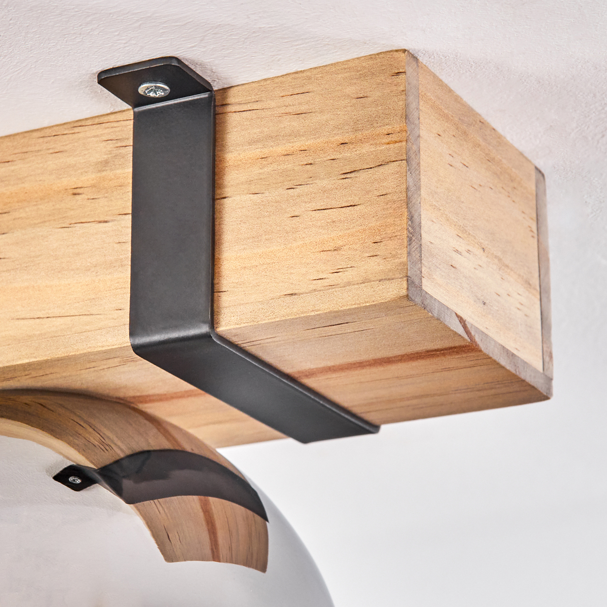 Nahaufnahme eines Holzbalkens, der von einer schwarzen Metallhalterung getragen wird, die an der Decke befestigt ist. Darunter ist ein gebogenes Objekt zu sehen.
