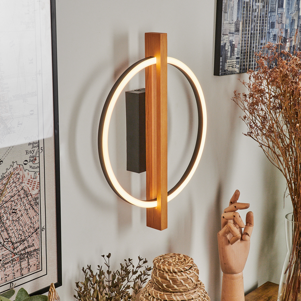 Eine moderne Wandleuchte mit Holzrahmen und kreisförmigem Licht. Eine Karte, Stadtlandschaftskunst und eine Holzhand sind im Hintergrund.